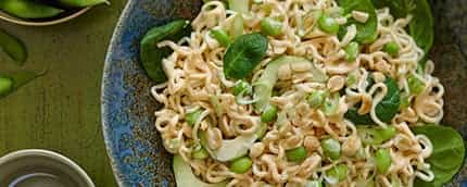 Overhead shot of ramen noodles with green onions and peas in a blue ceramic bow