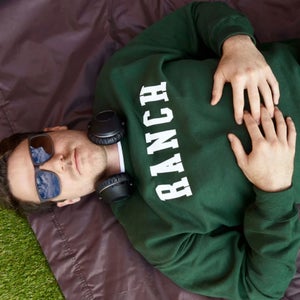 man lying down with headphones around his neck wearing a green Ranch sweatshirt